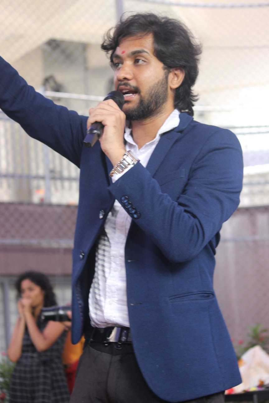 Akshay hosting on stage in a navy blazer